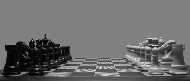 Side shot of a chess board with both sides in their starting positions facing each other. It's One Side Against the Other